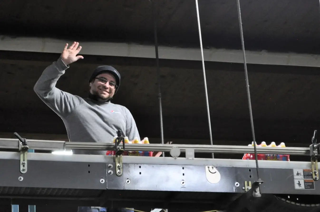 a man standing at a packing assembly line waving to the camera