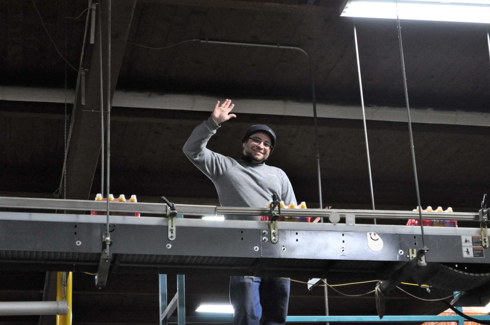 a man standing at a packing assembly line waving to the camera