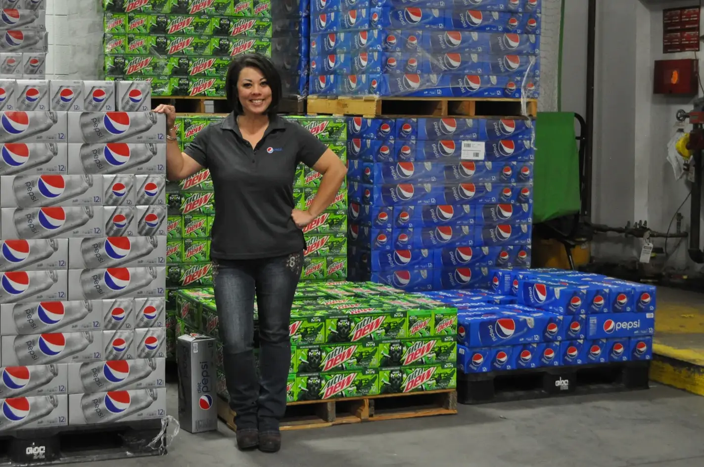 a woman smiling with palets of soda cases behind her