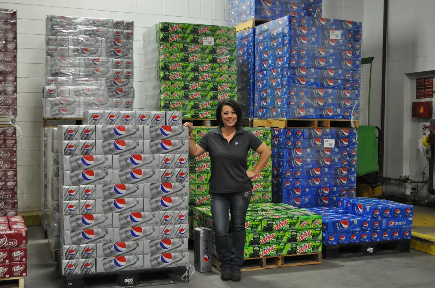 a woman smiling with pallets of soda cases behind her