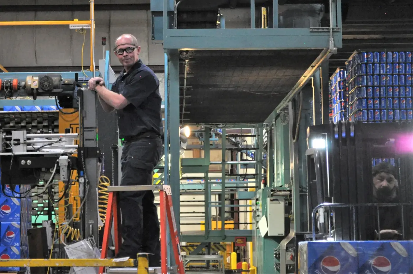 a man on a ladder working on packaging equipment