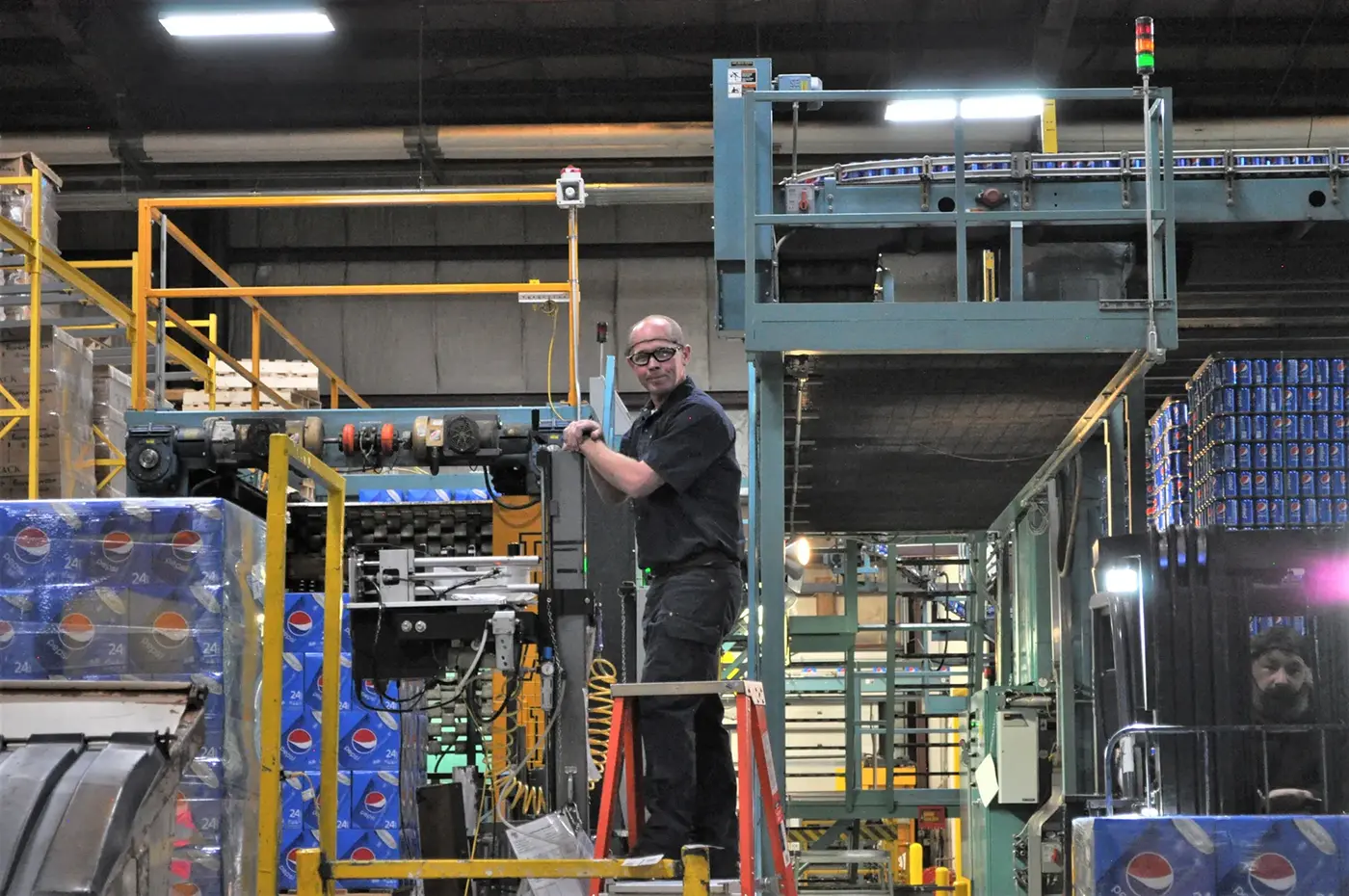 a man on a ladder working on packaging equipment